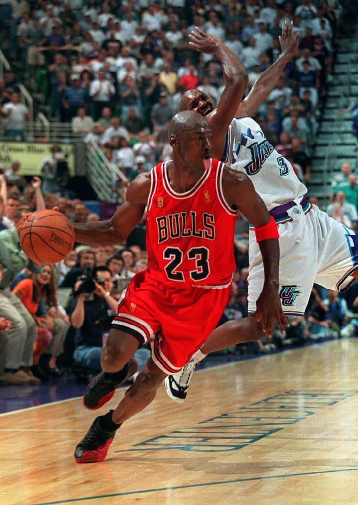 SALT LAKE CITY, UNITED STATES:  Michael Jordan (#23) of the Chicago Bulls sticks out his tongue as he goes past Bryon Russell of the Utah Jazz 11 June 1997 during game five of the 1997 NBA Finals at the Delta Center in Salt Lake City, Utah. Jordan scored 38 points as the Bulls defeated the Jazz 90-88 to take a 3-2 lead in the best-of-seven series.   AFP PHOTO/Jeff HAYNES