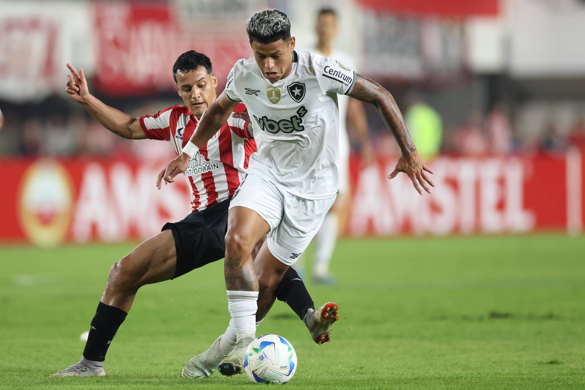 Matheus Martins, do Botafogo, conduz a bola marcado por jogador do Estudiantes