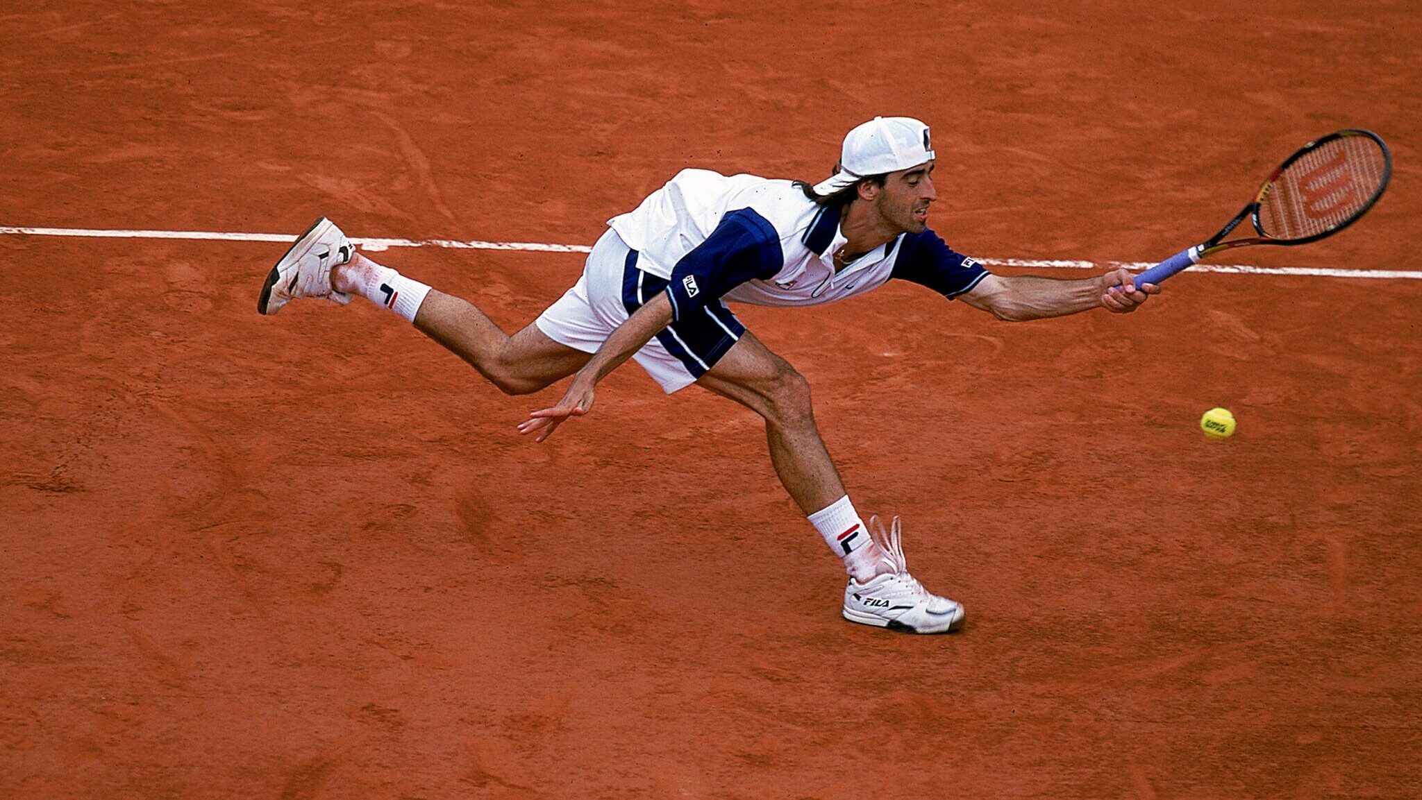 Fernando Meligeni estica a raquete para tentar alcançar bola em jogo de tênis em quadra de saibro