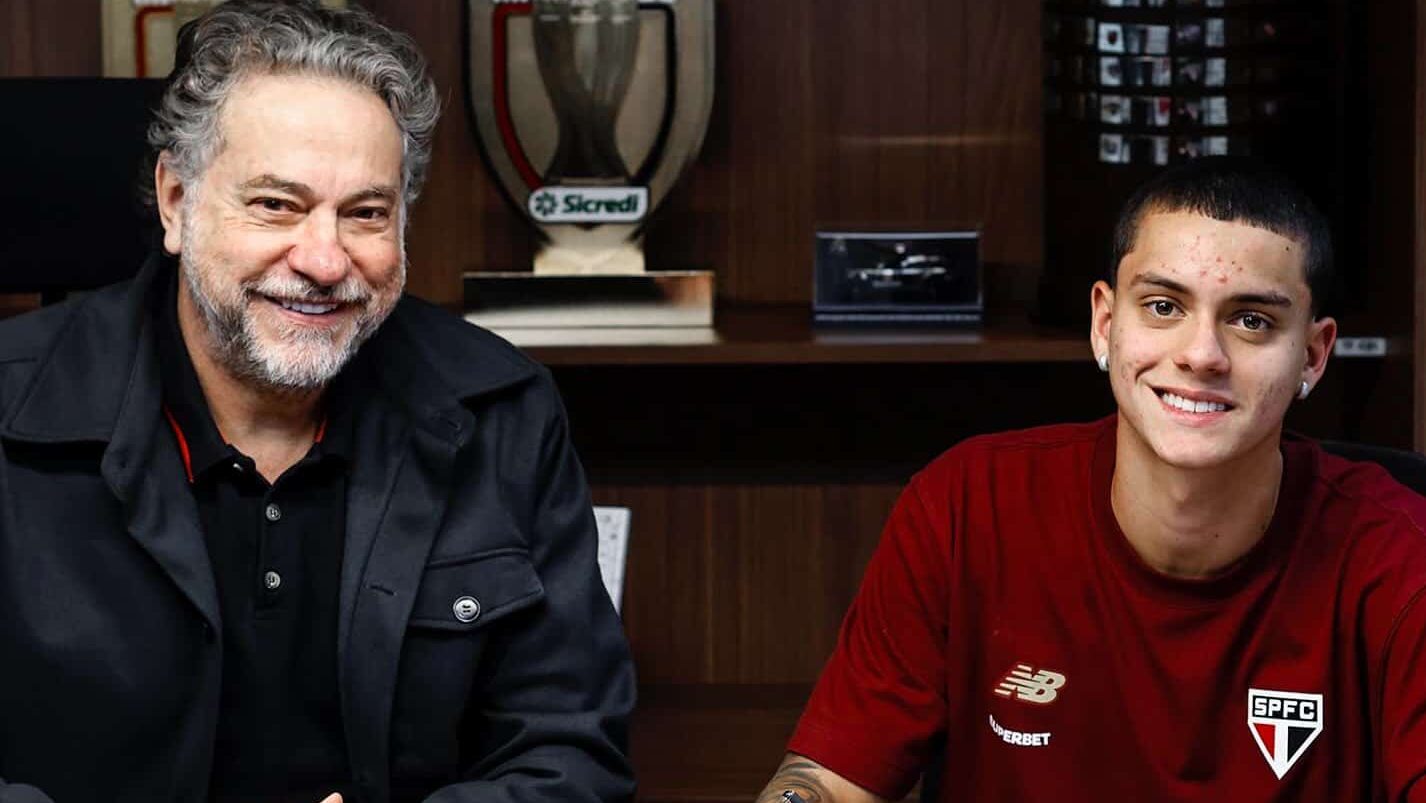 Lucca, jogador do São Paulo, está ao lado do presidente Julio Casares, os dois estão sentados em uma mesa